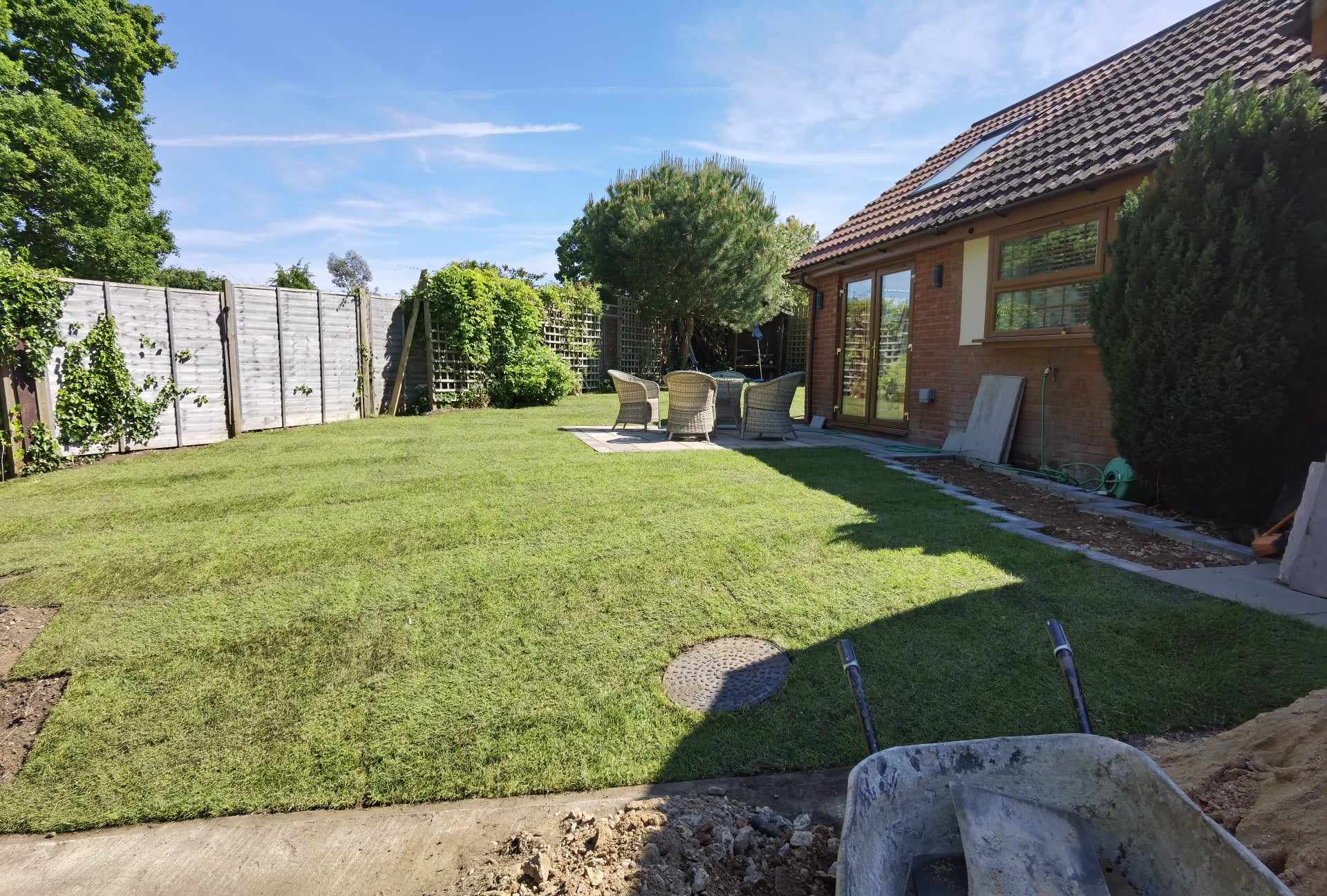 Completed garden transformation Suffolk — Finished garden with newly laid turf, construction materials visible indicating recent landscaping work completed