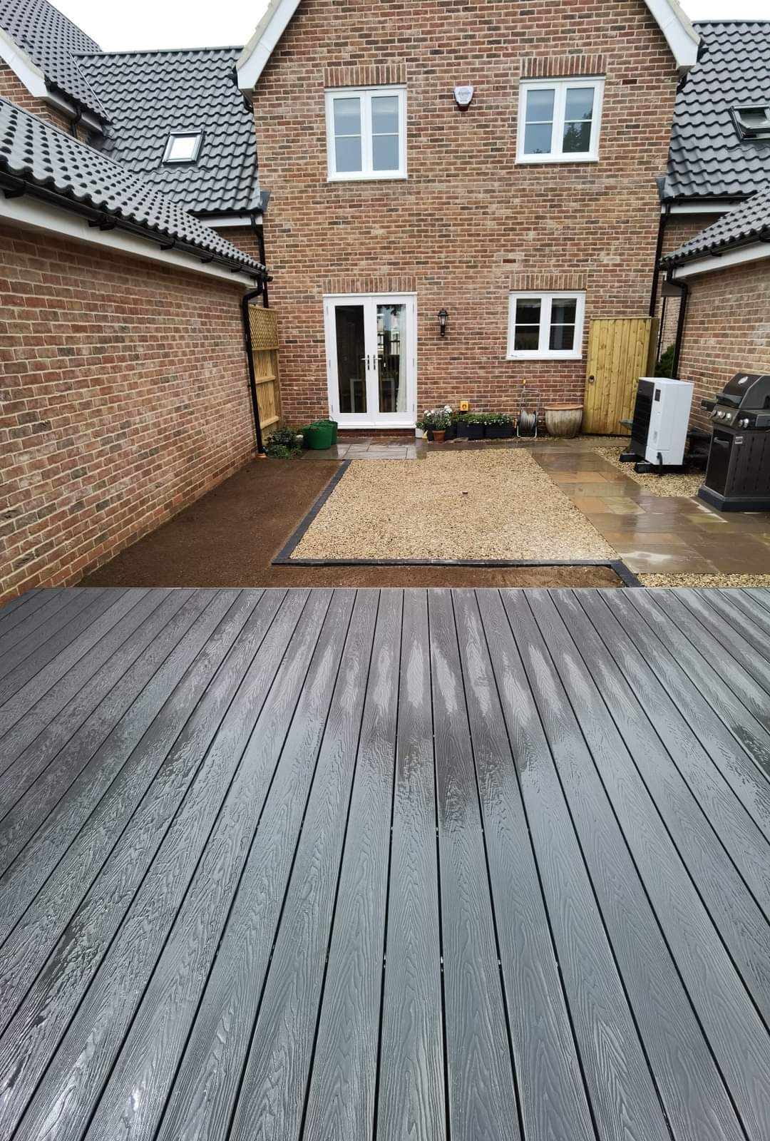 Decking installation Suffolk — Grey composite decking dominates foreground with gravel courtyard and brick house beyond