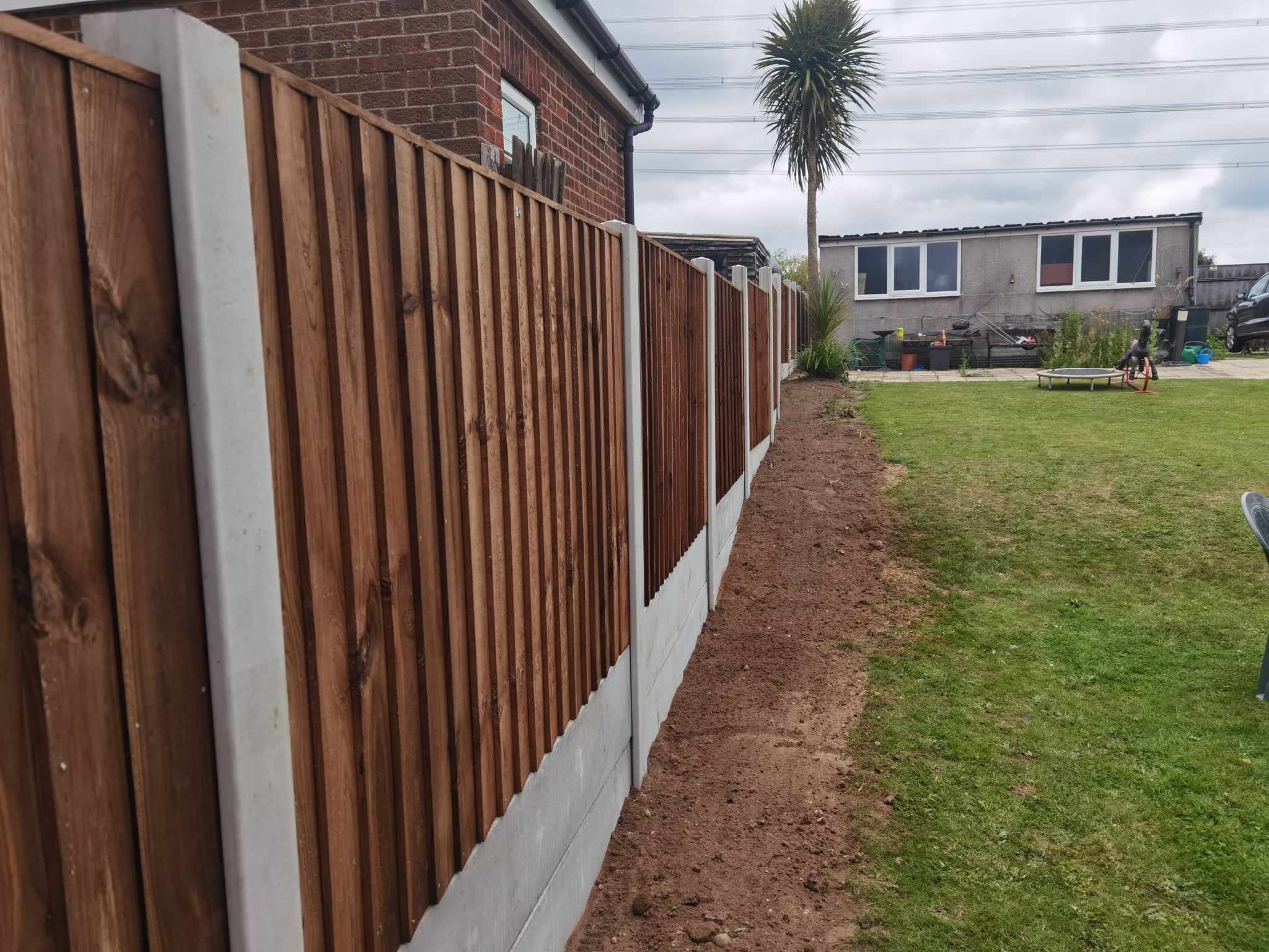 Fencing & gates Suffolk — Newly installed corrugated metal fencing with white base running along garden perimeter