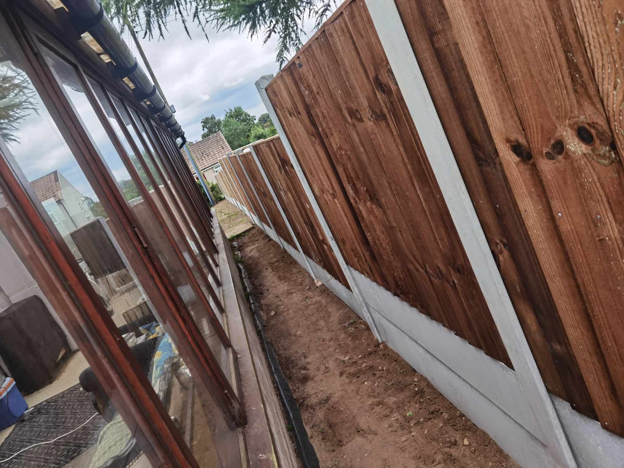 Fencing & gates Suffolk — Wooden fence installation with white base trim along narrow pathway