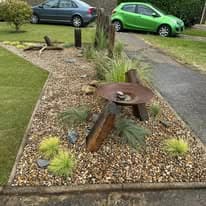 Flower bed design Suffolk — Landscaped flower bed with gravel, plants, and decorative metal sculpture feature