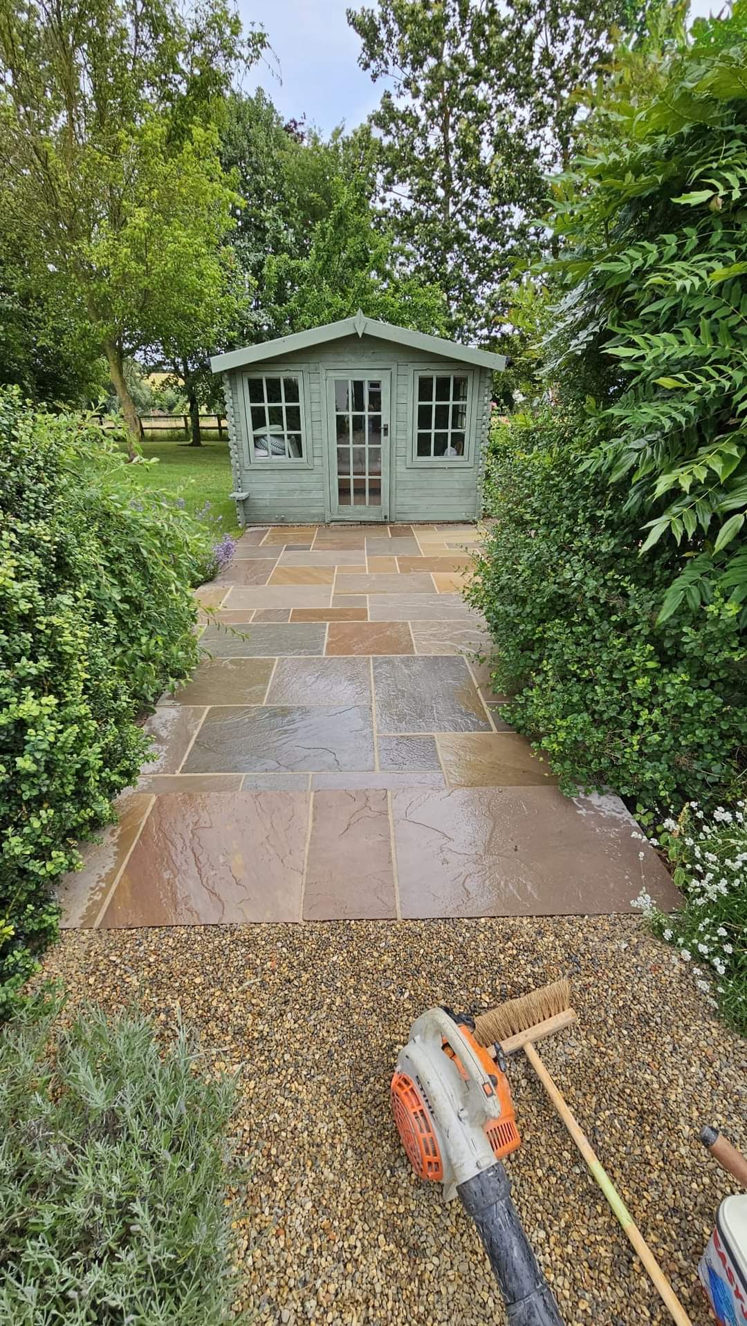 Patio installation Suffolk — Indian sandstone patio pathway with hedge borders leading to garden shed