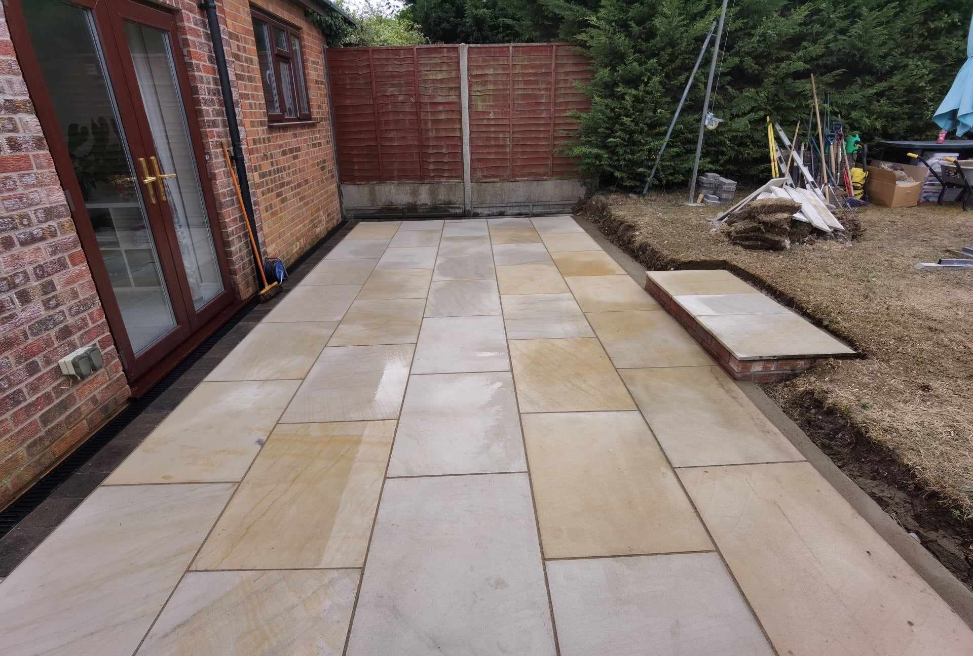 Patio installation Suffolk — Newly laid Indian sandstone patio with mixed warm tones adjacent to brick house