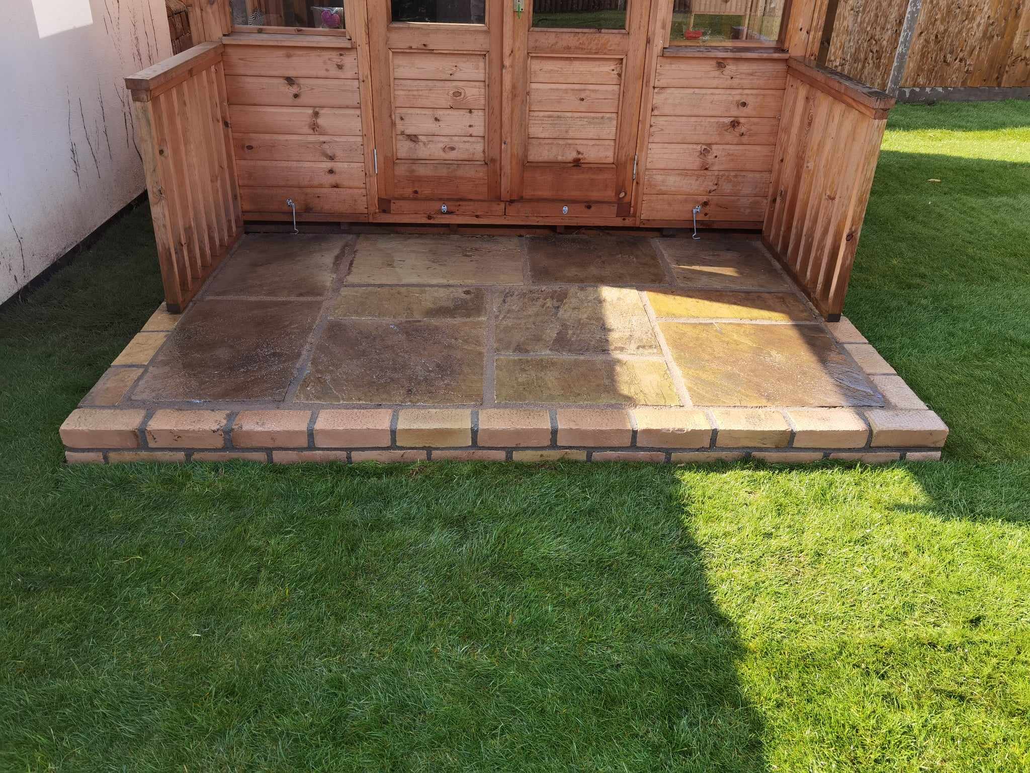 Patio installation Suffolk — Brick and stone paved patio area with wooden garden structure backdrop