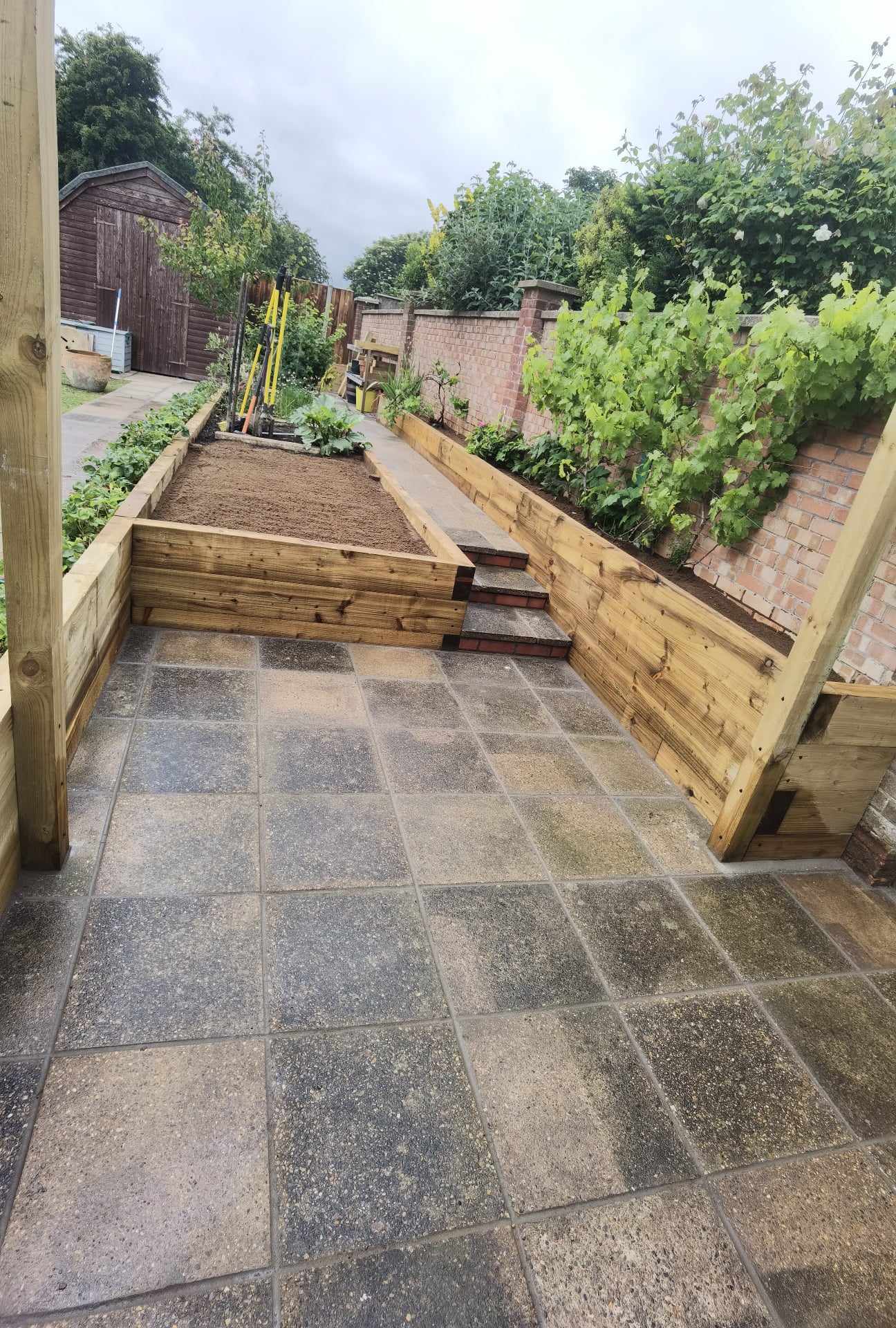 Patio installation Suffolk — Stone slab paved patio area with raised wooden beds and garden beyond
