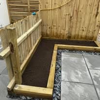 Raised bed garden Suffolk — Wooden raised bed garden construction with dark soil, fencing backdrop visible