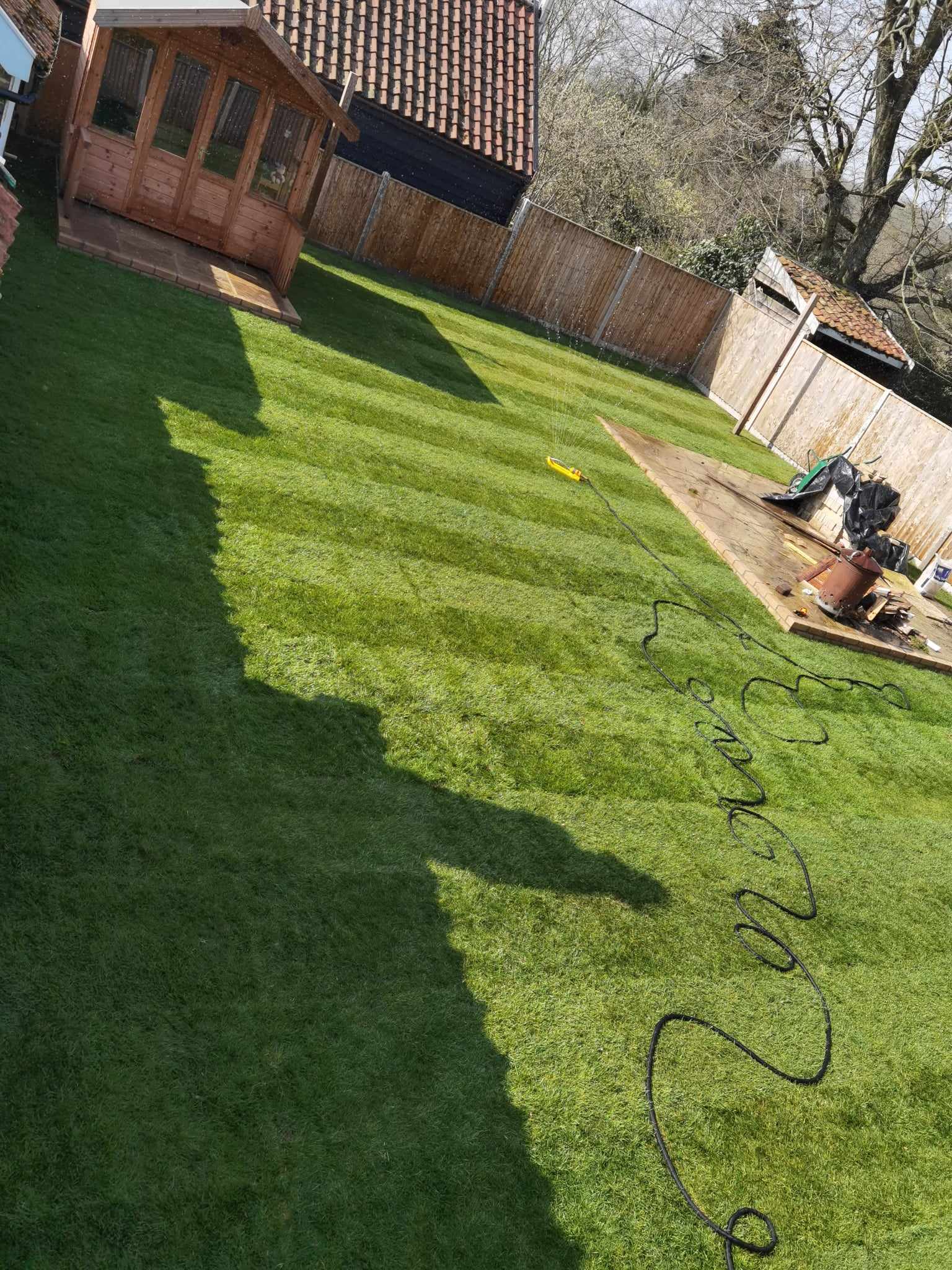 Turfing & lawn Suffolk — Large freshly laid real grass lawn with garden hose visible